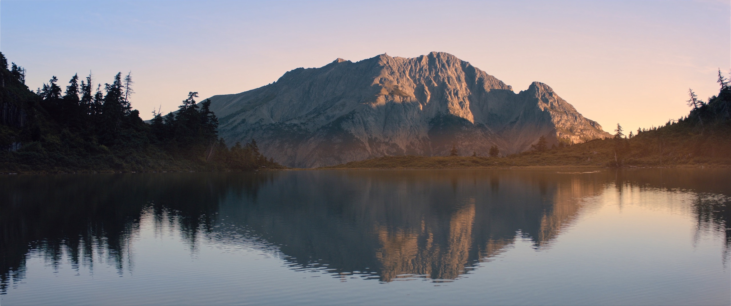 A calm alpine lake at sunrise reflecting a mountain in still water